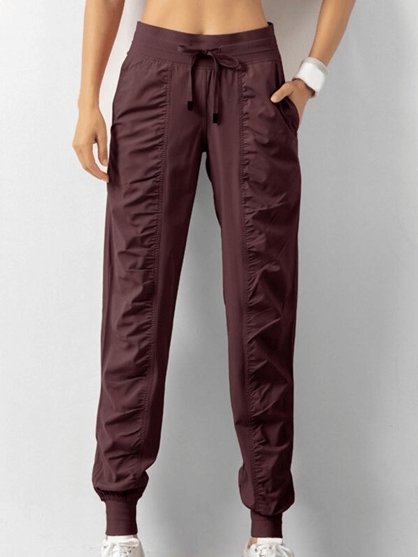 Women's sports joggers with side pockets and cuffs in solid color, featuring a drawstring waist, pleated front, and a relaxed fit.